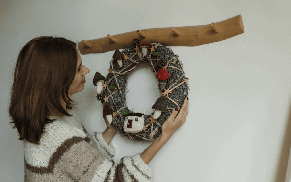 A woman hanging a wreath on the wall with an accent of a wooden hook