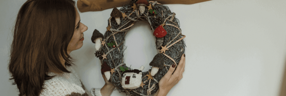 A woman hanging a wreath on the wall with an accent of a wooden hook