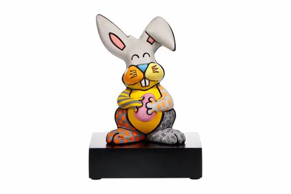 Un lapin en porcelaine peint à la main avec une expression joyeuse, un patchwork coloré en orange, jaune et gris, sur une base noire élégante.