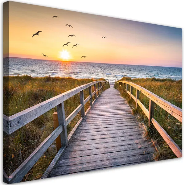 Wooden boardwalk leading to the beach at sunset with seagulls flying over the ocean and tall grass along the path.