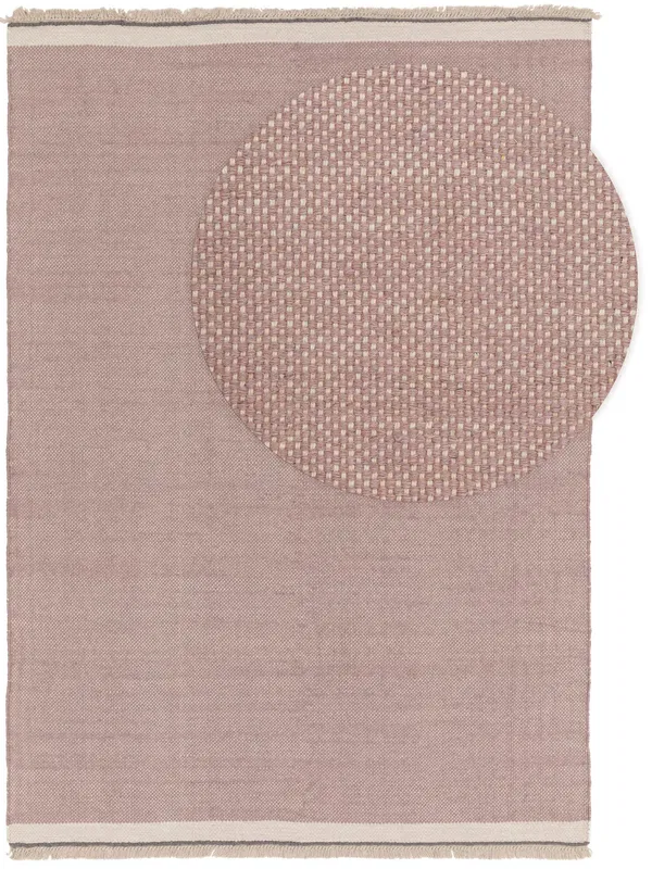 Soft pink rug with a woven circular pattern on one corner, offering a minimalist design with fringe edges.