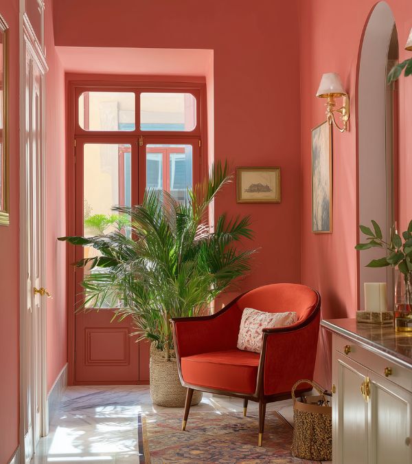 Stylish hallway with red walls and armchair, surrounded by lush green plants for bold interior design inspiration