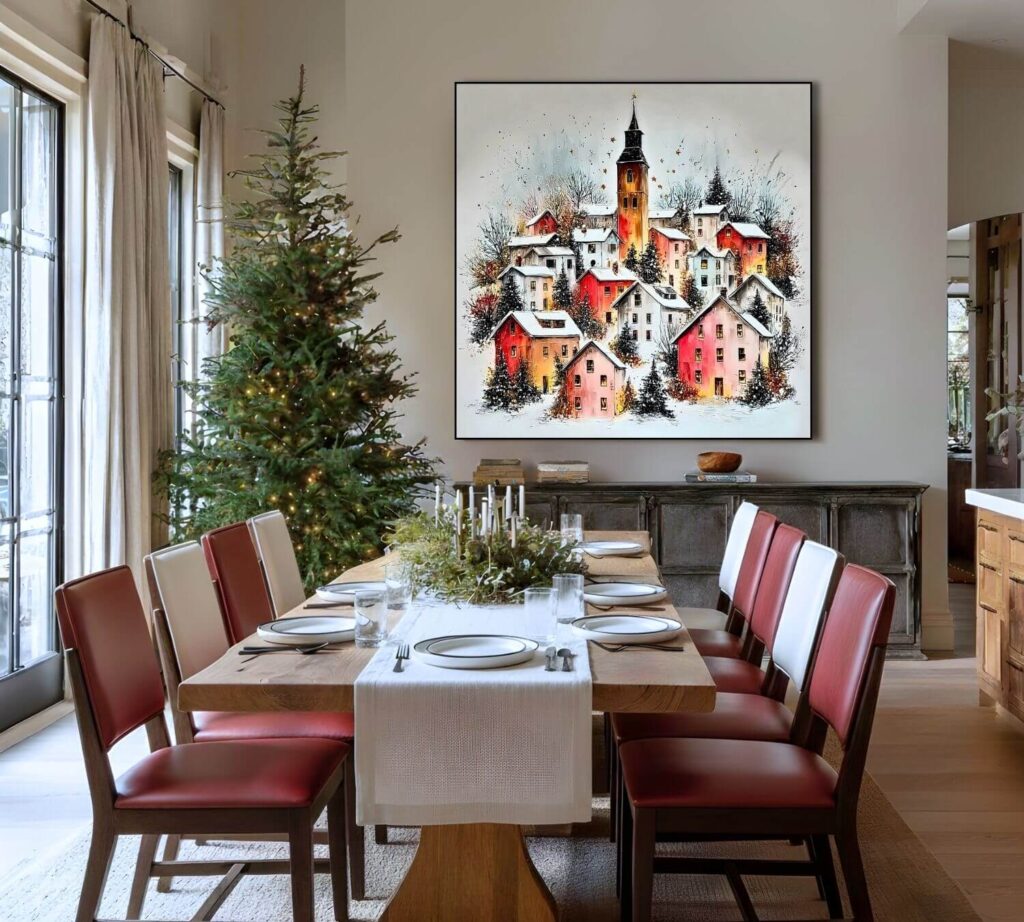 A painting of a snowy European town square hung in a dining room featuring a wooden table, red chairs, and a decorated Christmas tree.
