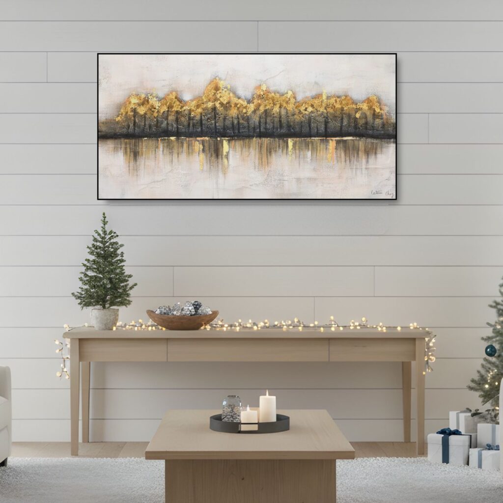 A landscape-oriented painting with a shimmering gold and dark grey horizon line, centered over a light wood console table decorated with small Christmas trees.