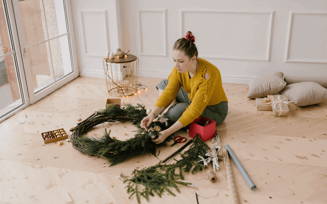 a woman wearing a yellow sweat shirt decorating a green wreath